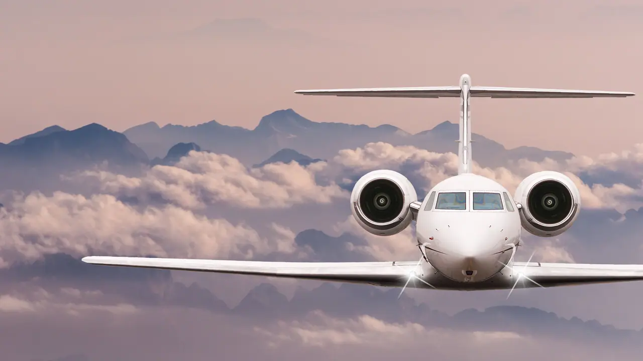 Private jet in flight above mountains and cloud at dusk