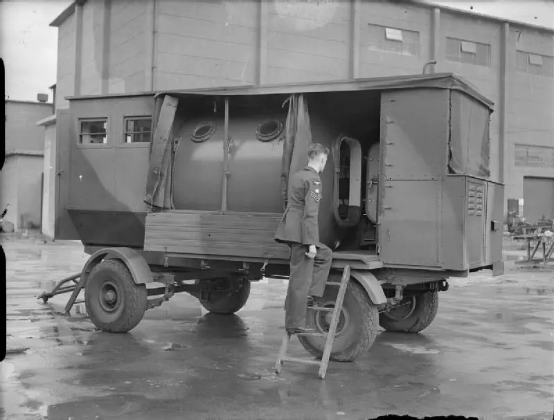 A sergeant at the open door of a mobile decompression chamber on a wheeled trailer at the Royal Aircraft Establishment, Farnborough, in the Second World War
