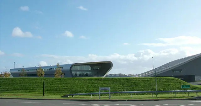 The curved aluminium-clad terminal building at Farnborough Airport beside a grass bank, with part of a hangar roof on the right