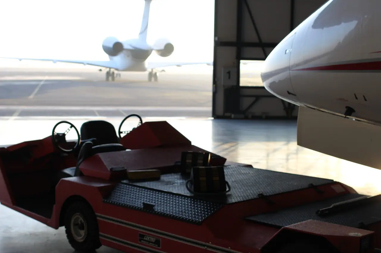 A private jet on the apron, seen from inside the hangar past an aircraft tug