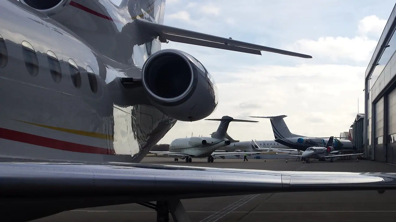 Private jets on the apron beside a hangar, seen from beneath the tail of another jet